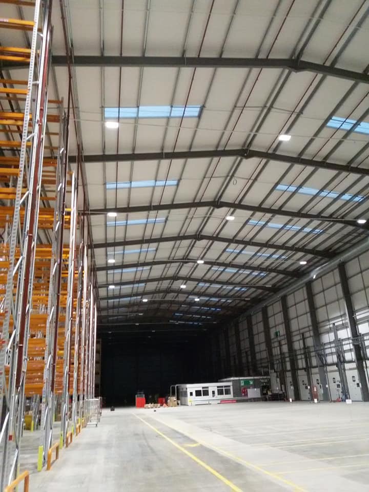 A long warehouse aisle lit from end to end by high-level lighting