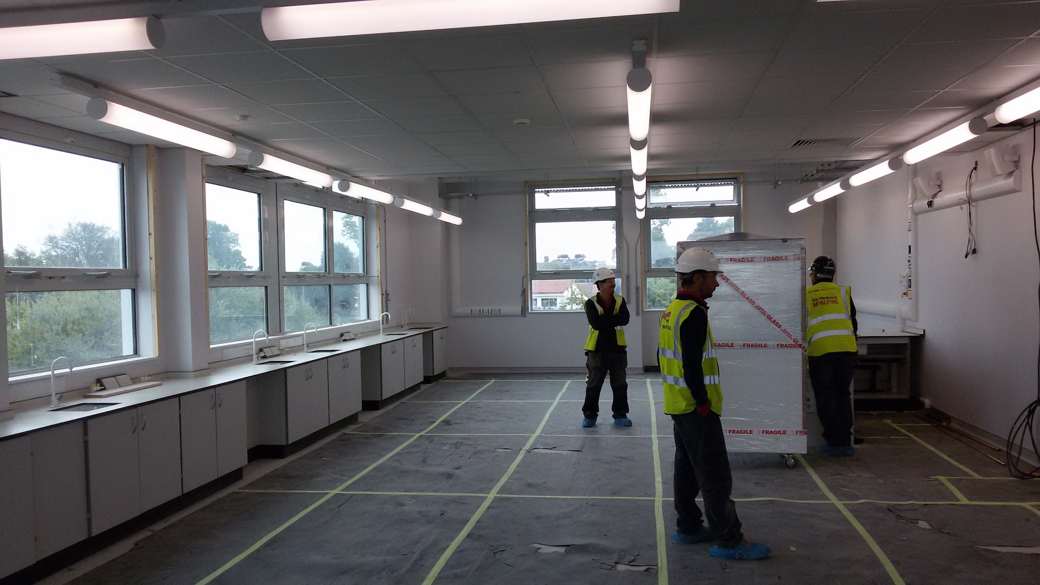 A room being fitted out with new ceiling lighting, three workers in hi-vis in the middle of the floor